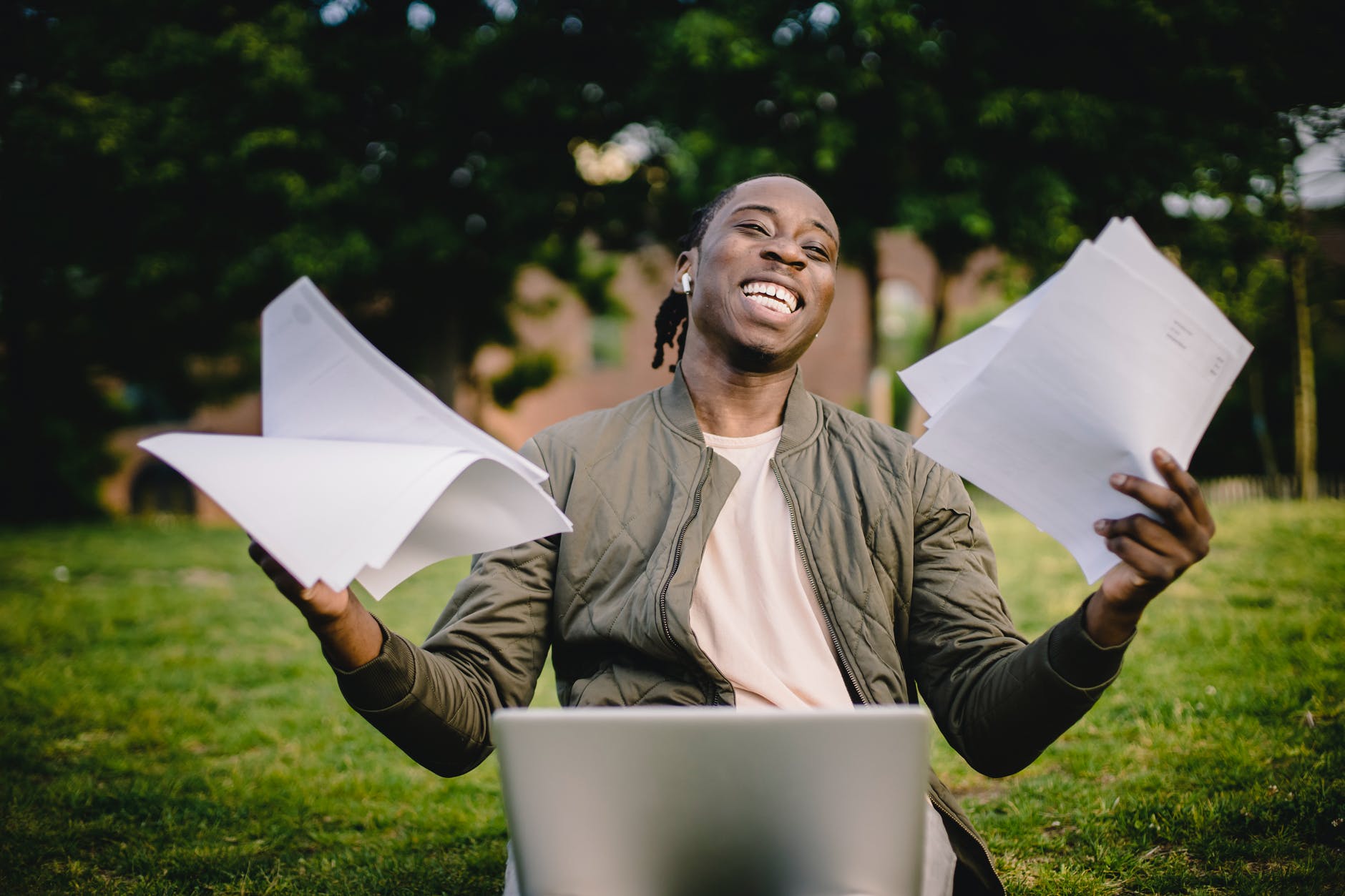 happy african american man holding sheets of paper in front of laptop